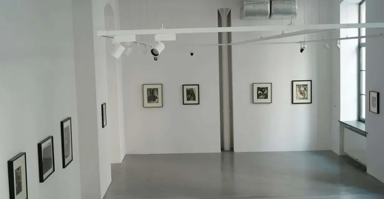 Galeria sztuki z pracami Karola Hillera. Wnętrze z białymi ścianami, szarą podłogą i kilkoma czarno-białymi fotografiami na ścianach.